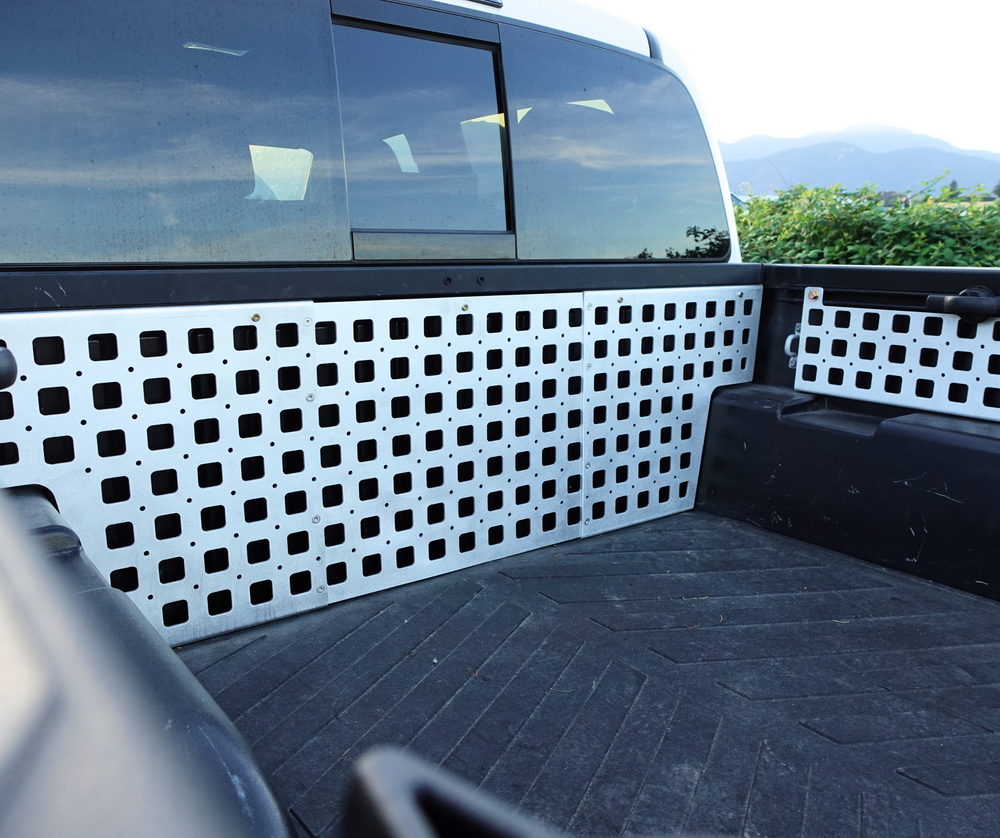 White metal panels installed on a truck bed interior designed for modular storage and attachment, featuring multiple square cutouts, identified as BPF 05-23 Tacoma bed Molle panels.