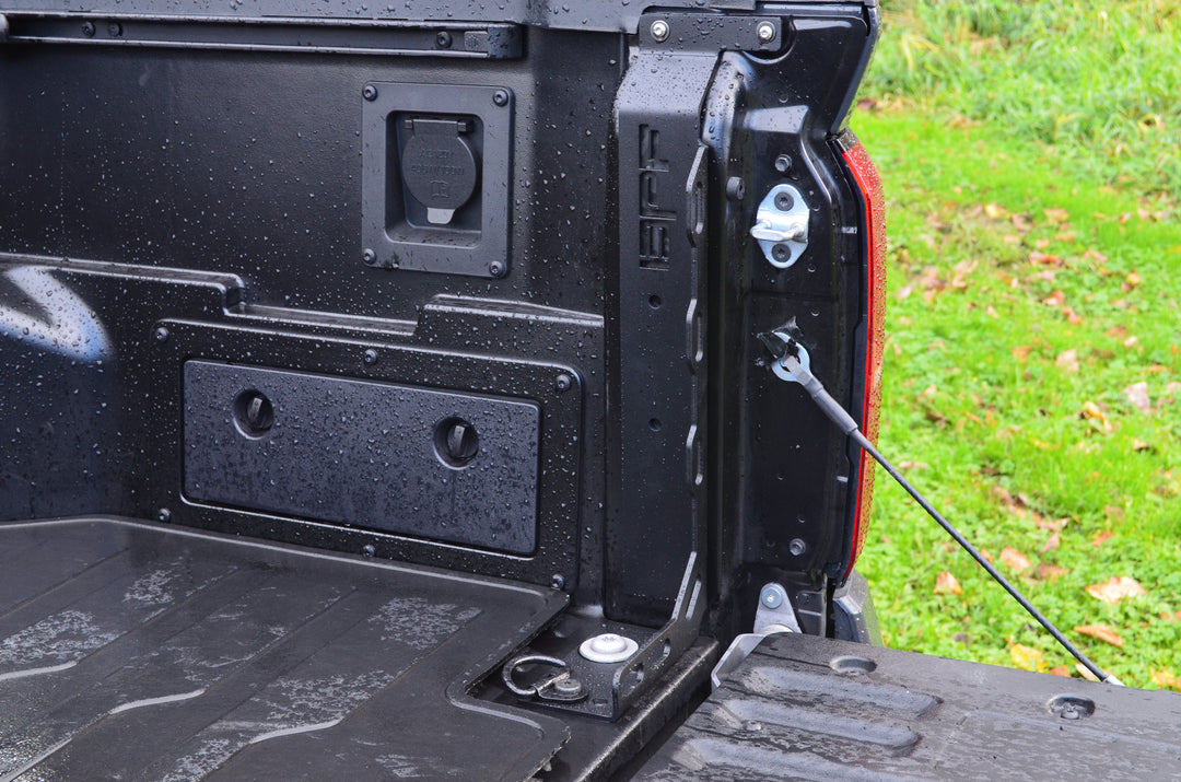 Close-up view of the black powder-coated truck bed corner with BPF 2024-2025 Toyota Tacoma Bed Stiffeners installed, showing heavy-duty CNC fabricated metal components on a wet surface.