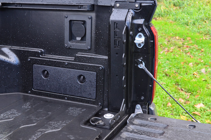 Close-up view of the black powder-coated truck bed corner with BPF 2024-2025 Toyota Tacoma Bed Stiffeners installed, showing heavy-duty CNC fabricated metal components on a wet surface.
