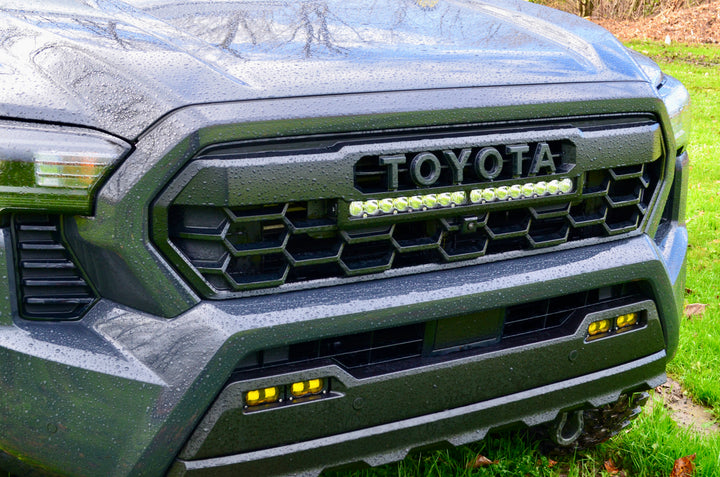 Close-up of a wet black truck front featuring the 2024 Trailhunter Grille with BPF letters installed, showcasing a rugged hexagonal grill mesh and integrated LED light bar.