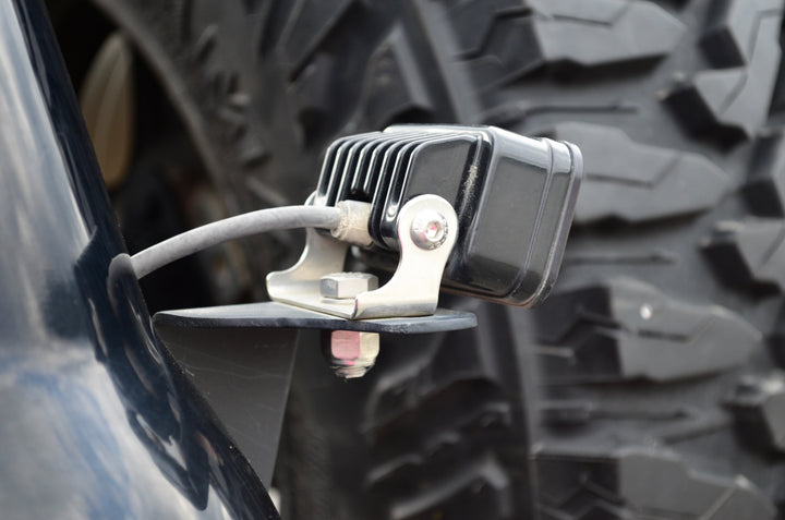 Close-up image of a mounted LED light attached with BPF 80 series Land Cruiser rear light brackets 92-97, showing durable metal bracket and wiring near a rugged tire.