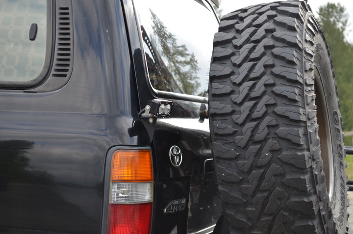 Close-up of a black Land Cruiser showing the BPF 80 series Land Cruiser rear light brackets 92-97 installed near the rear light and spare tire mount.