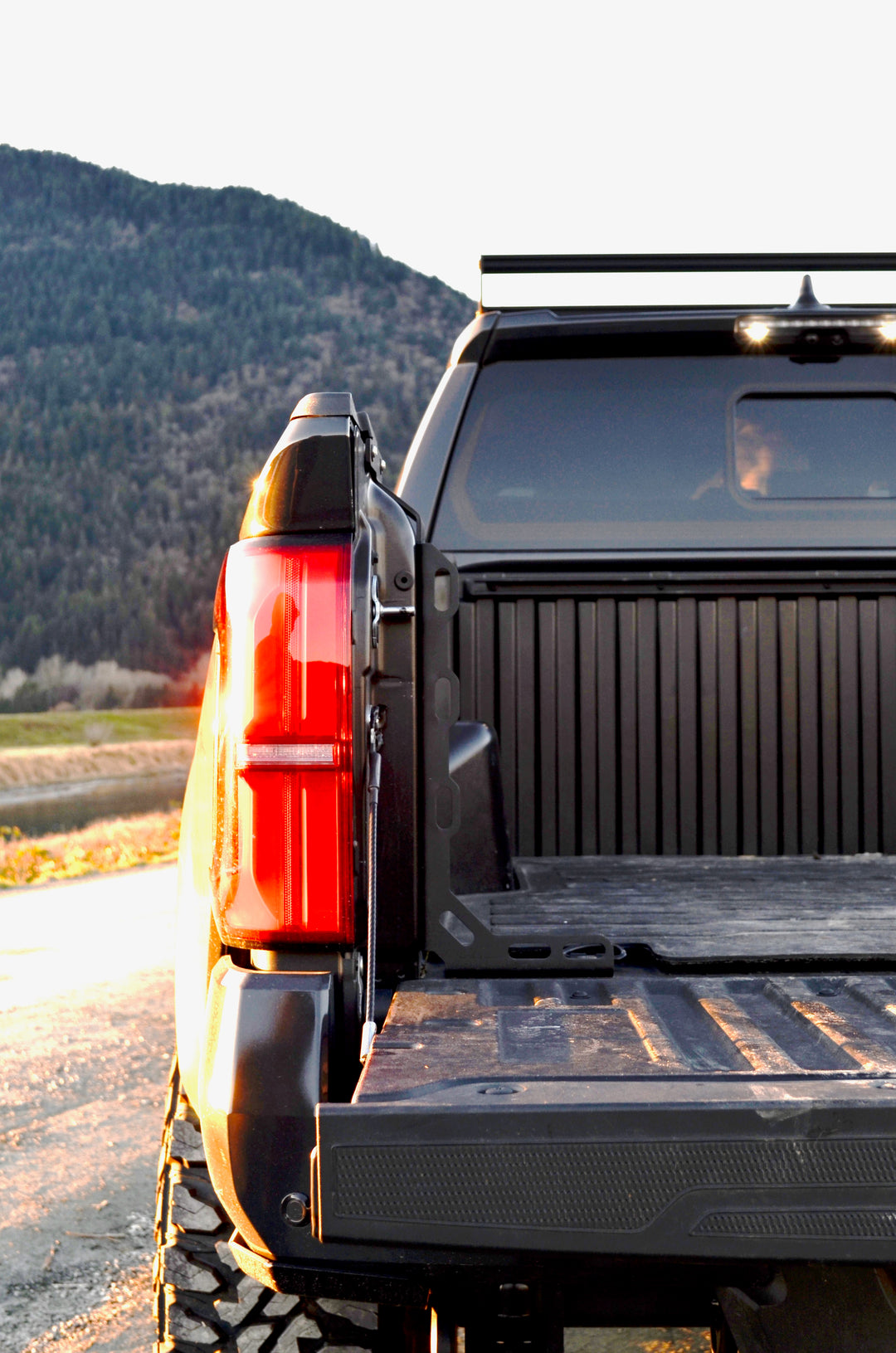 Rear view of a black Toyota Tacoma truck bed featuring installed BPF 2024-2025 Toyota Tacoma Bed Stiffeners with mountainous landscape in the background at sunset.