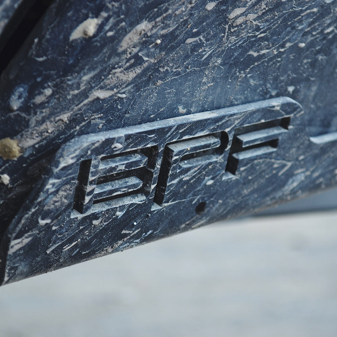 Close-up of a scratched and dirty metal plate embossed with the letters BPF on a rugged surface.