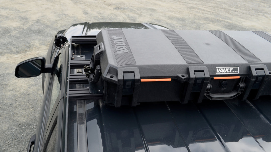 BPF Universal Pelican Vault V700 Case Mounting brackets securing a large black Pelican Vault case on the roof rack of a dark vehicle for overlanding gear storage.