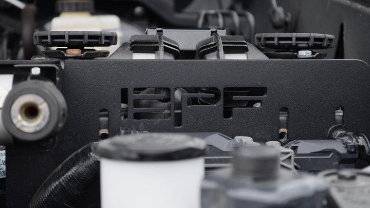Close-up of a black metal BPF 2024-2025 Tacoma and Land Cruiser Twin Compressor Mount installed in a vehicle engine bay, featuring a powder-coated finish and CNC fabrication.