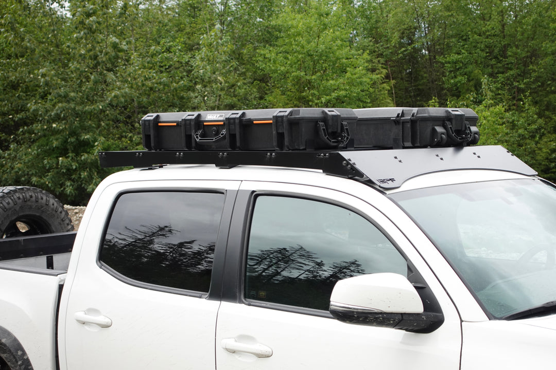 BPF Universal Pelican Vault V800 and V730 Case Mounting brackets securing a black protective case on a white truck roof rack with greenery in the background.