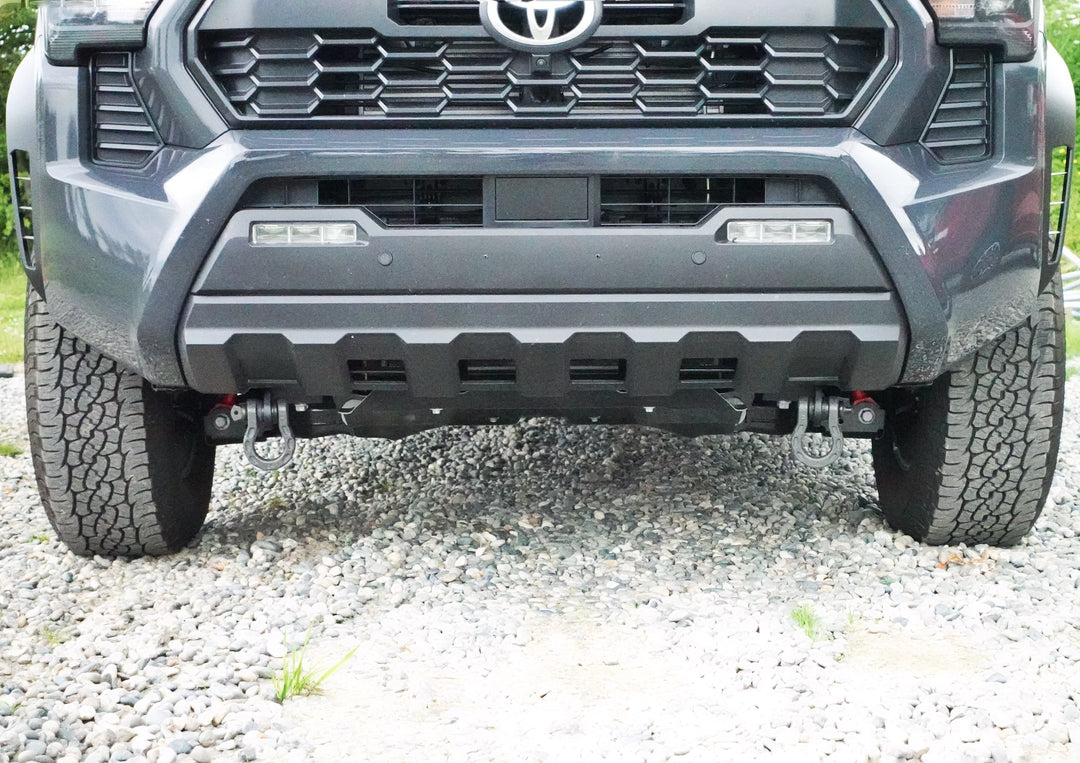 Front view of a gray Toyota Tacoma equipped with BPF 2024+ Tacoma Recovery Points mounted on the front bumper, featuring heavy-duty tow hooks on a gravel surface.