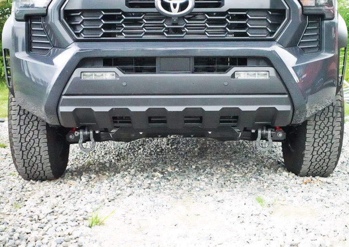 Front view of a gray Toyota Tacoma equipped with BPF 2024+ Tacoma Recovery Points mounted on the front bumper, featuring heavy-duty tow hooks on a gravel surface.