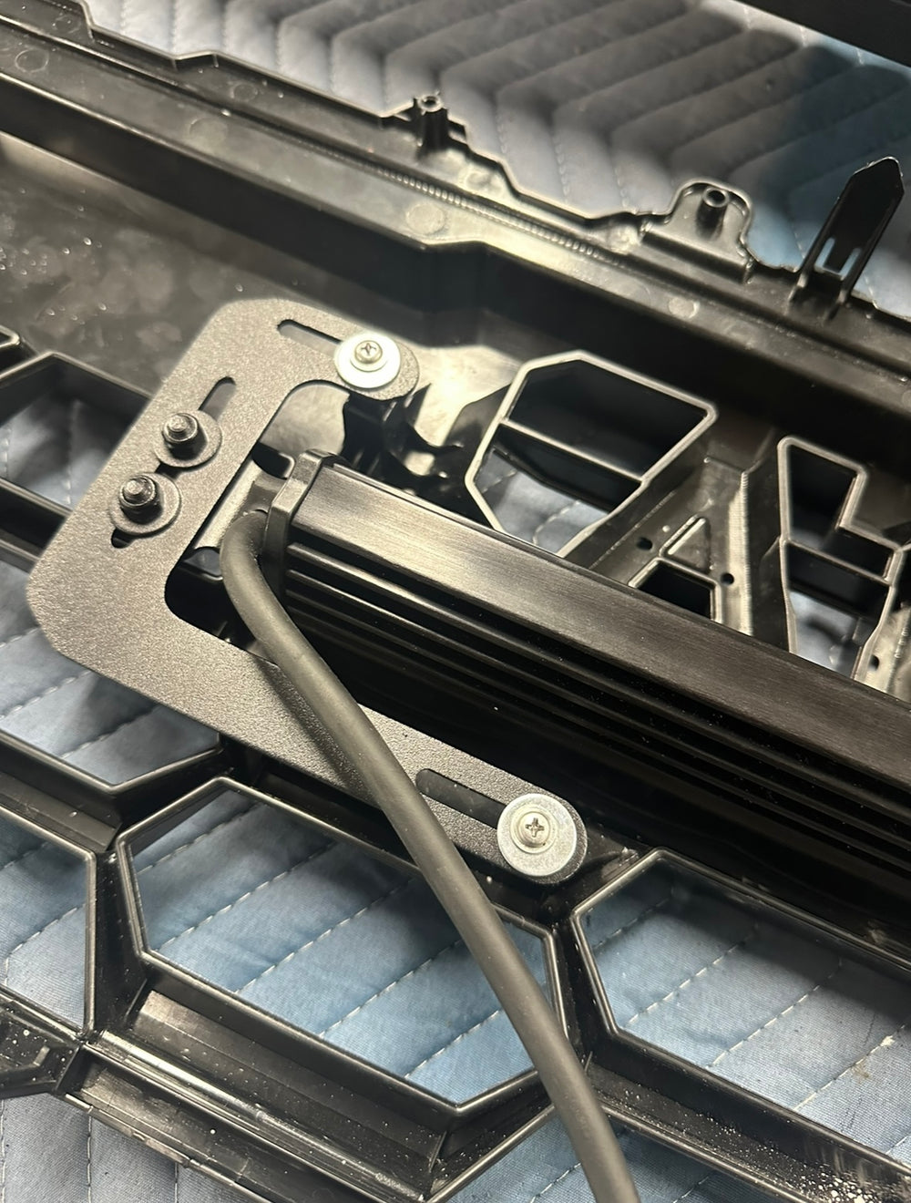 Close-up of a mounted light bar on a black metal bracket installed on a honeycomb-style vehicle grille, showcasing the BPF 2024+ Tacoma TRD Pro and Trailhunter Universal Light Bar Bracket.