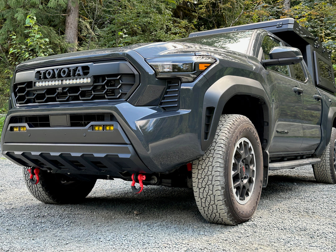 Close-up of a dark gray Toyota Tacoma featuring red BPF 2024+ Tacoma Recovery Points mounted on the front bumper, designed for heavy-duty towing and recovery.