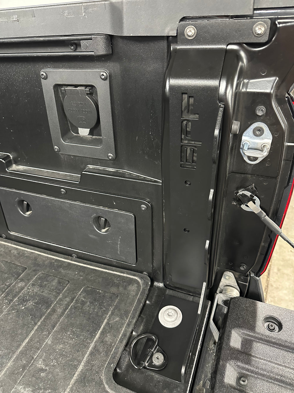 Close-up of a black metal BPF 2024-2025 Toyota Tacoma Bed Stiffeners installed in the truck bed corner, showing heavy-duty construction with mounting points and electrical connectors.