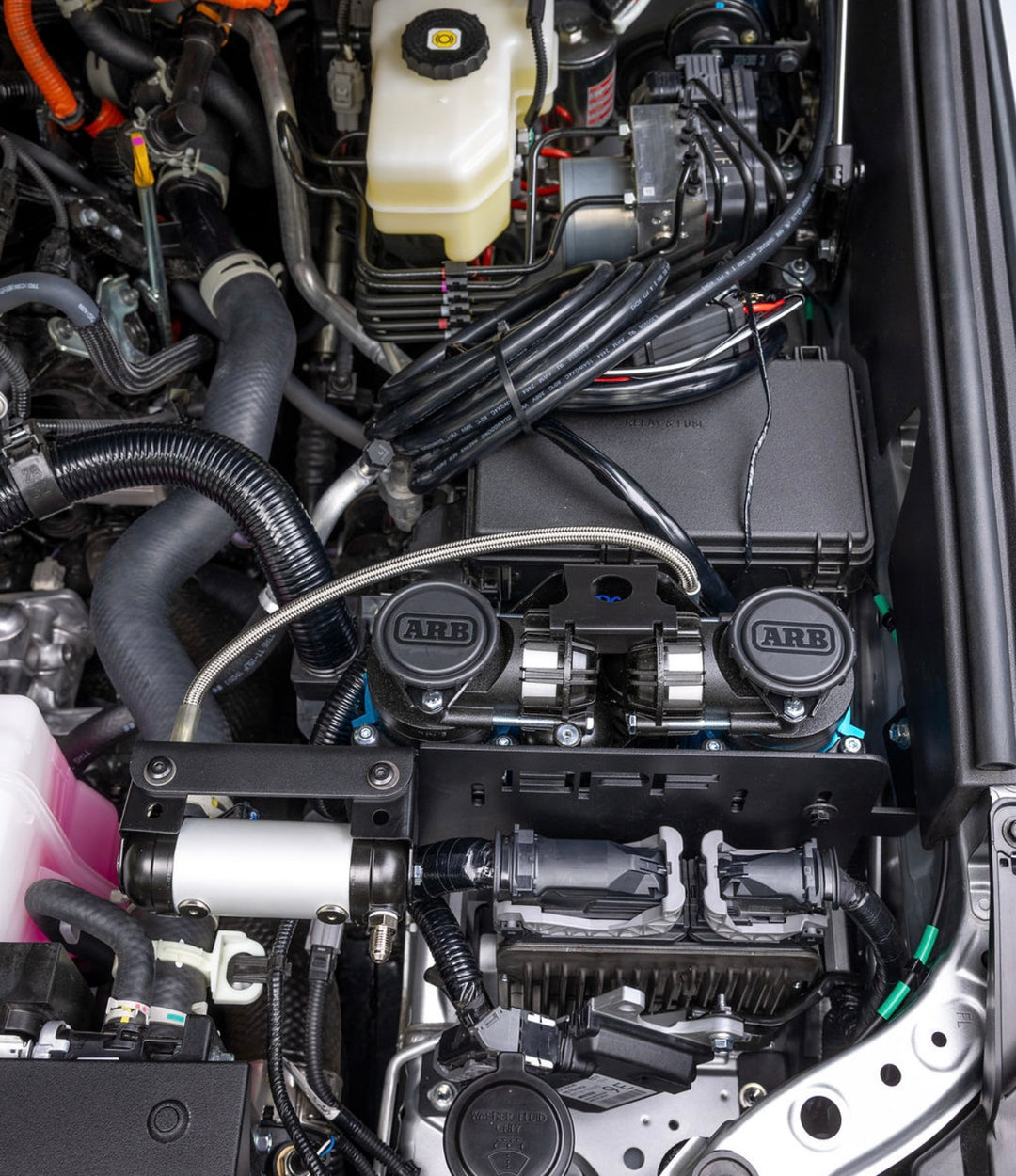 Close-up of an engine bay featuring the BPF 2025+ 4runner twin compressor mount with dual ARB compressors, surrounded by various hoses and electrical wiring in a clean, organized layout.