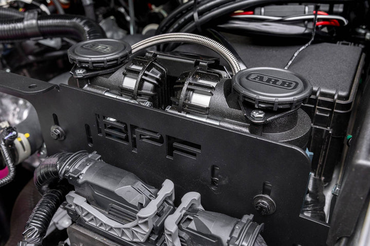 Close-up of a BPF 2025+ 4runner twin compressor mount installed in an engine bay, featuring two ARB compressors secured by a durable black mounting bracket with visible wiring.