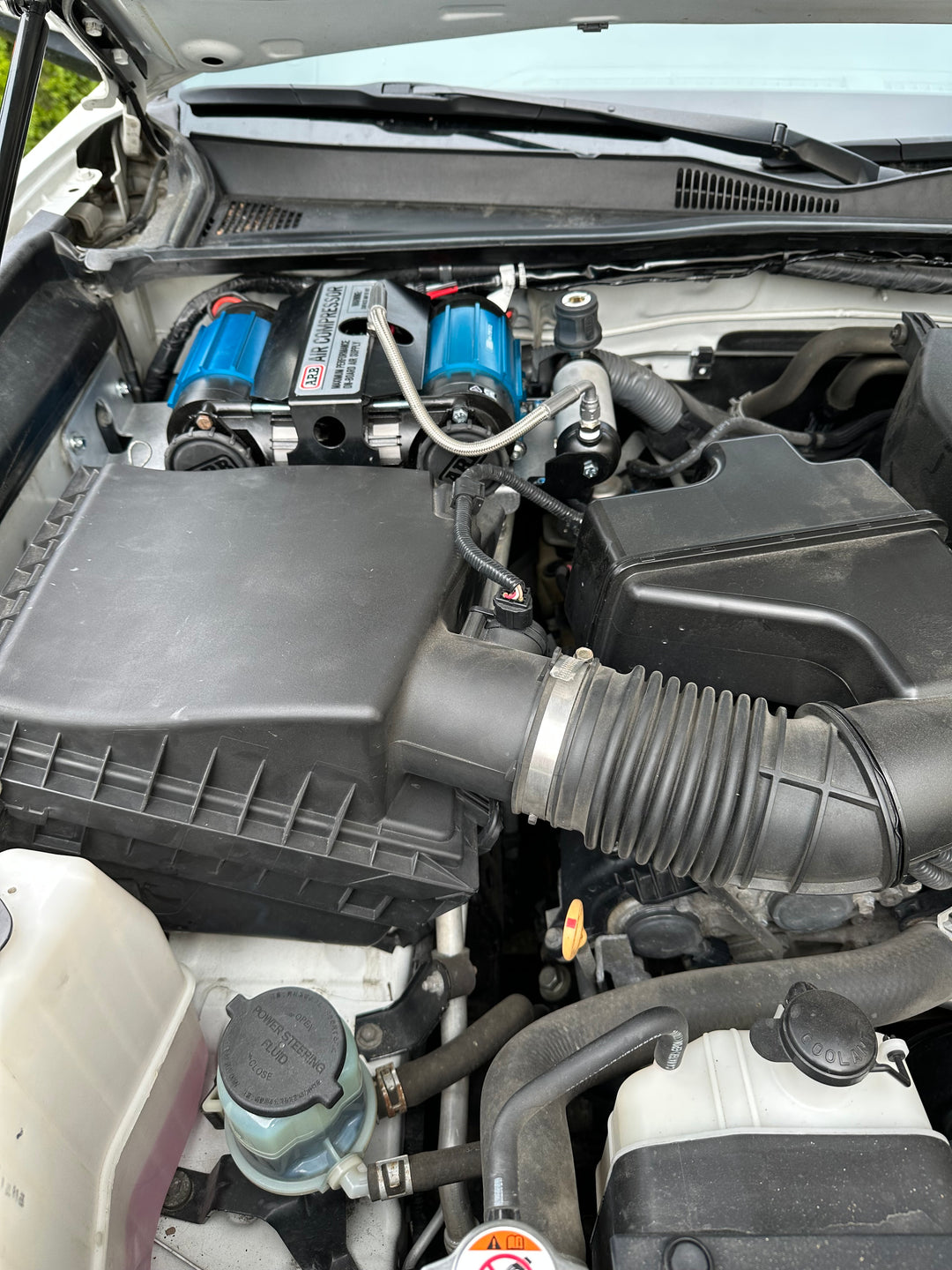 Engine bay featuring the BPF 2016-2023 3rd Gen Tacoma Compressor mount with blue compressors installed, showing a clean and organized setup with hoses and wiring in place.