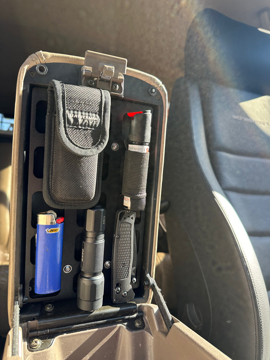 BPF 80 Series Land Cruiser/LX450 Center Console Molle Panel holding a lighter, flashlight, multitool, and pouch, installed inside a vehicle center console for organized storage.