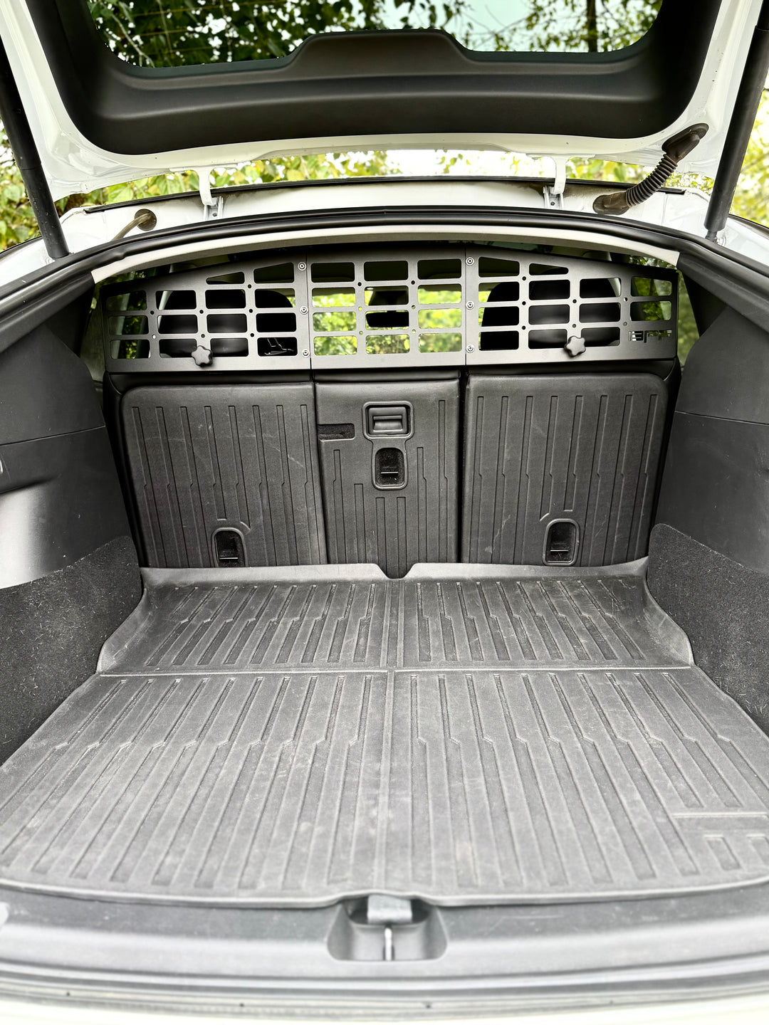 Cargo area of a Tesla Model Y equipped with a black BPF Molle Style Pet Barrier Tesla Model Y 2020-CURRENT installed behind the rear seats, featuring molle panels and a sturdy rubber cargo mat.
