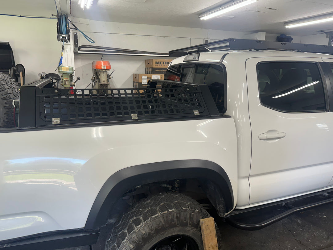 White 05-26 Tacoma truck equipped with a sturdy bed rack installed, showing the "05-26 Tacoma Bed Rack fits 2nd,3rd and 4th gen Tacomas" with a black powder-coated finish inside a garage.
