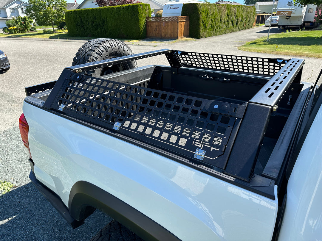 Close-up of a black metal bed rack with mesh panels installed on a white truck, designed as the 05-26 Tacoma Bed Rack fits 2nd,3rd and 4th gen Tacomas, ideal for overlanding and heavy-duty use.