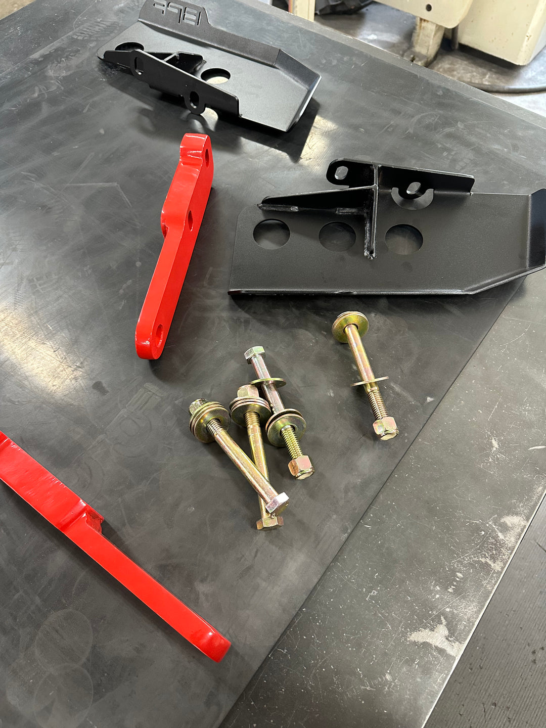 BPF 4th gen Tacoma rear tow hooks with integrated skid plates displayed with mounting bolts and hardware on a workshop surface, featuring powder-coated metal parts.