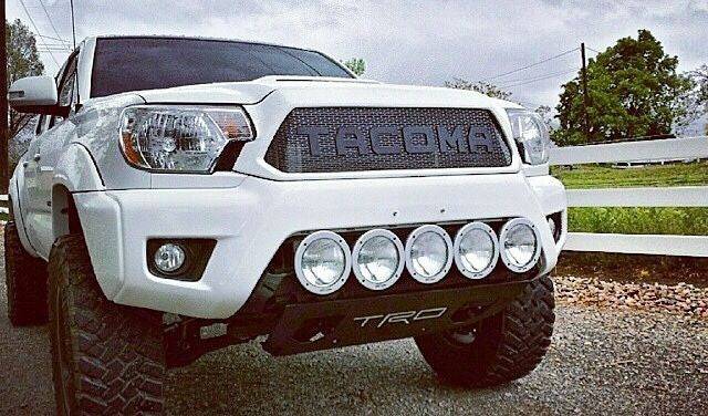 White Toyota Tacoma with BPF Completed 2012-2015 Toyota Tacoma Grill featuring a powder-coated grill mesh and robust front bumper with five round off-road lights and TRD skid plate.