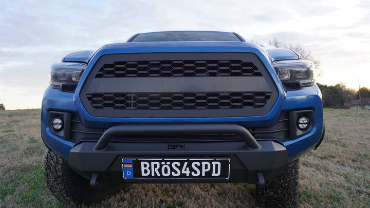 Front view of a blue Toyota Tacoma equipped with a BPF 2016-2023 Toyota Tacoma Grill featuring a rugged black honeycomb mesh design and a heavy-duty front bumper with an integrated bull bar.