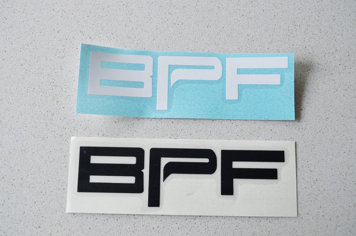 Two rectangular Sticker - BPF decals, one in white on a blue backing and the other in black on a white backing, displayed on a light gray surface.