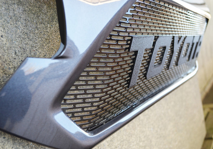 Close-up of a black mesh grille featuring bold texture and "TOYOTA" lettering installed on a vehicle, showcasing the BPF 2012-2015 Toyota Tacoma Mesh and Lettering accessory.