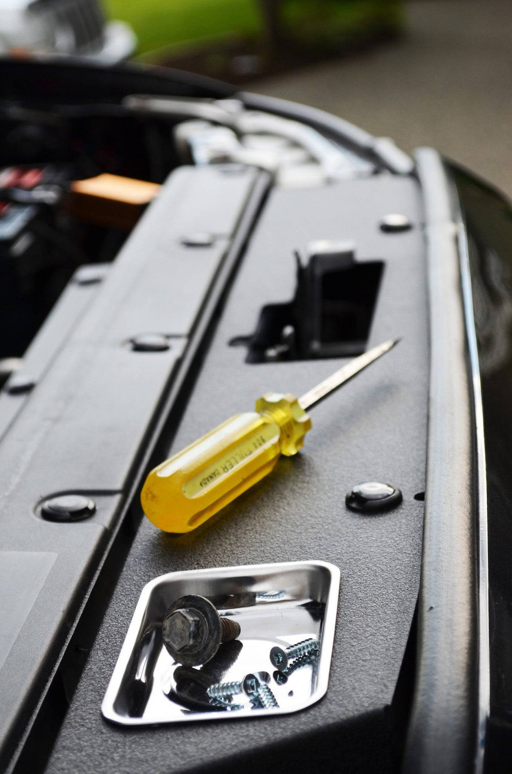 Close-up of a yellow-handled screwdriver and metal screws on the BPF 05-11 Toyota Tacoma Radiator Cover during installation or maintenance.