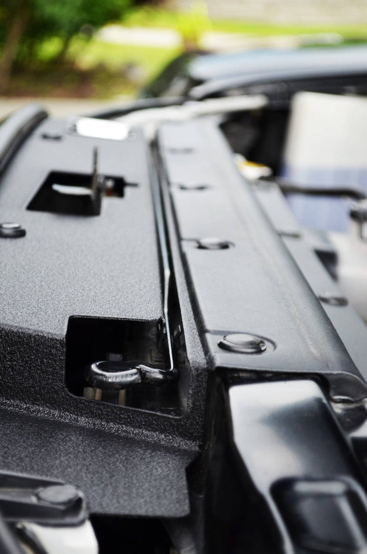 Close-up view of a textured black metal BPF 05-11 Toyota Tacoma Radiator Cover installed under the hood, showcasing its CNC fabricated design and durable powder-coated finish.