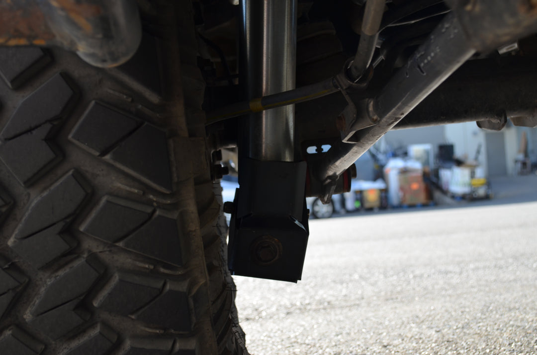 Close-up view of a heavy-duty shock guard installed near the suspension of a rugged off-road tire on a vehicle, featuring the BPF 4runner 04-24/FJ 07-14 Shock Guards designed for durable protection.