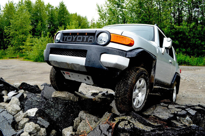 Off-road vehicle with BPF Completed 2007-2014 FJ Cruiser Grill navigating rocky terrain surrounded by green trees under daylight.