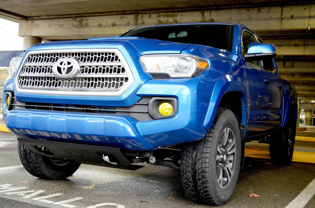 Blue Toyota Tacoma with a visible BPF 2016-2023 Tacoma Skid Plate installed underneath, parked in an indoor garage setting.