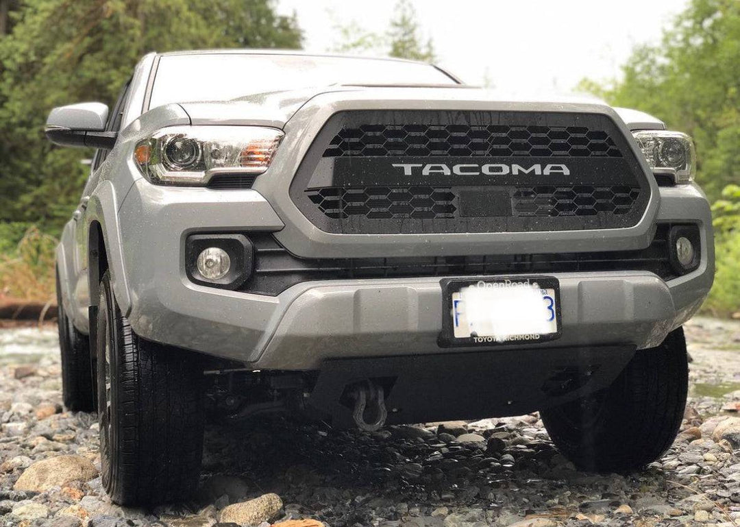 Front view of a silver Toyota Tacoma equipped with a BPF 2016-2023 Toyota Tacoma Grill featuring a bold black honeycomb mesh design and integrated "TACOMA" lettering.