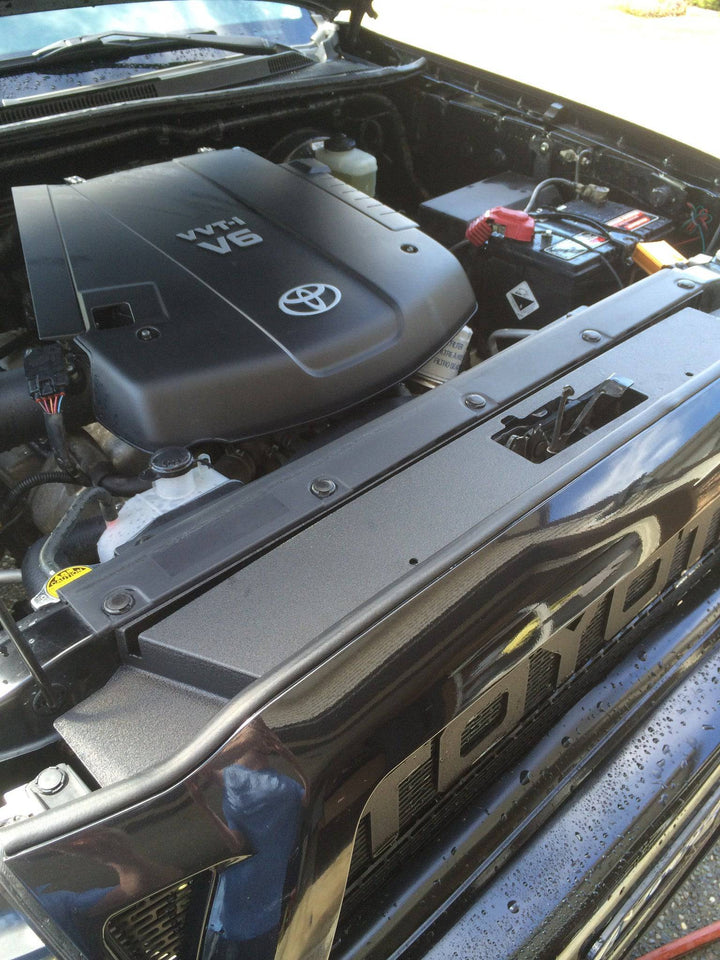 Close-up view of a black BPF 05-11 Toyota Tacoma Radiator Cover installed in a truck engine bay featuring clean, durable CNC fabricated construction with OEM fitment and powder-coated finish.