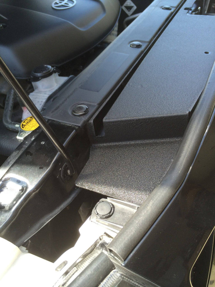 Close-up view of a textured black BPF 05-11 Toyota Tacoma Radiator Cover installed in a vehicle engine bay, showing a clean, precise fit and durable surface finish.