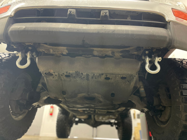 Underside view of a vehicle showing the BPF 3rd gen 4Runner Tow Hook Set 1996-2002 installed on the front bumper with heavy duty hooks attached.