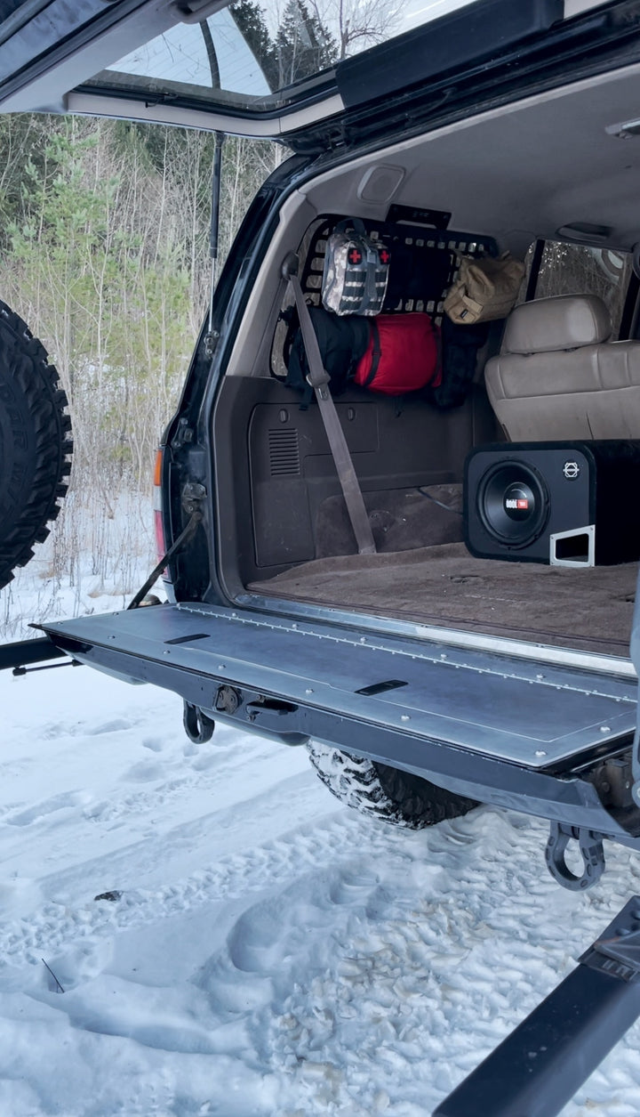 Open tailgate on an off-road vehicle showcasing organized gear and cargo with the BPF 80 Series Land Cruiser and LX450 Tailgate Storage in a snowy outdoor setting.