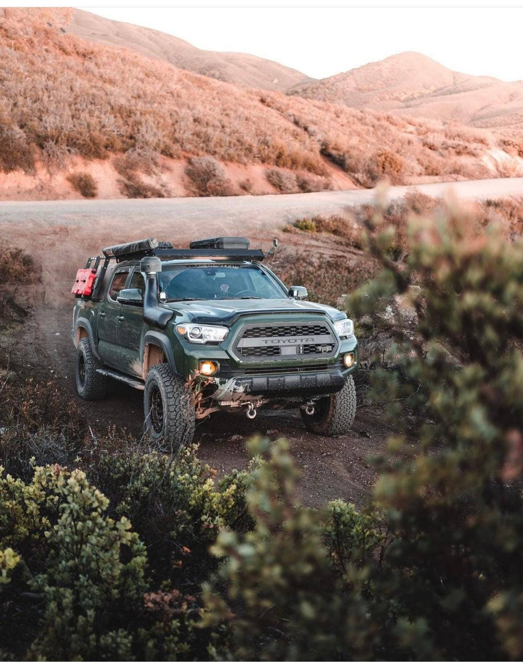 Off-road Toyota Tacoma featuring a rugged front with BPF 2016-2023 Toyota Tacoma Grill, equipped for adventure with off-road tires, roof rack gear, and front tow hooks.